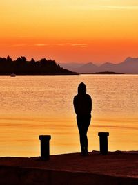 Rear view of silhouette man standing by sea against orange sky