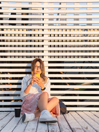 Woman with cup of coffee meets sunset on wooden pier. female with curly hair  listens to music