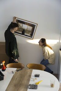 Boyfriend hanging picture frame by cheerful girlfriend in living room