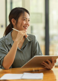 Portrait of a smiling young woman using digital tablet while sitting on table