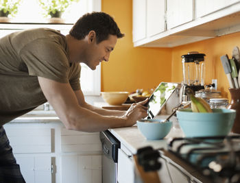 Smiling man using tablet while standing in kitchen at home