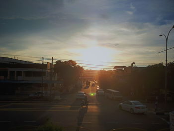 Cars on city street against sky during sunset