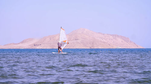 Man learns to ride on a board with a sail, windsurfing. windsurfing on the crystal clear water. 