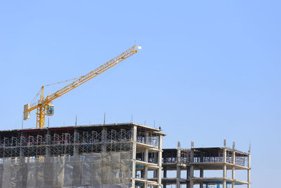 Crane by building against clear blue sky