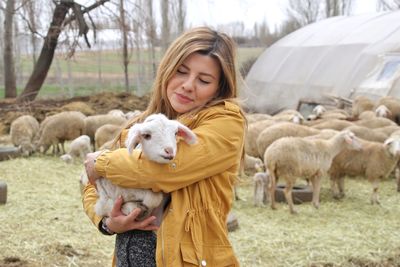 Woman carrying lamb while standing at farm