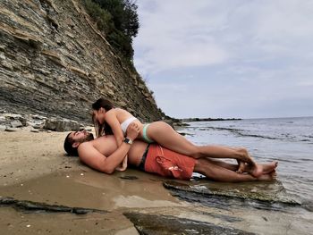 Young woman sitting on rock at beach against sky