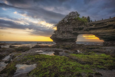 Rock formation on beach against sky during sunset