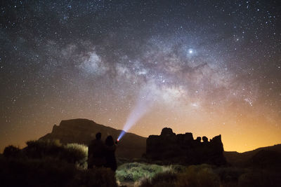 Silhouette couple with flashlight standing against star field