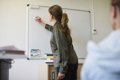 Female doctor writing on whiteboard while explaining teenager during therapy session