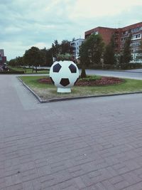 Soccer ball on field by footpath against sky in city