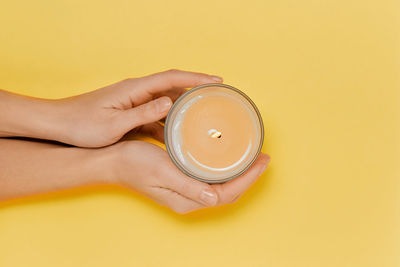 Cropped hand of woman holding bottle against yellow background