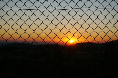 Silhouette chainlink fence on field against sky during sunset