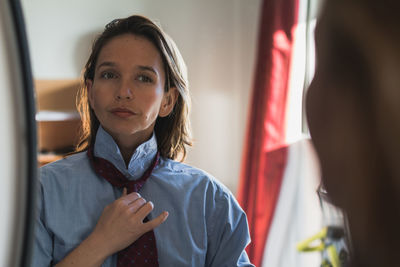 Reflection of confident woman adjusting necktie on mirror