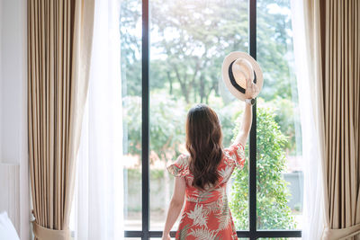 Rear view of woman looking through window at home