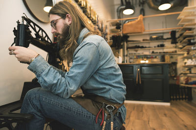 Side view of shoemaker adjusting sewing machine at workshop