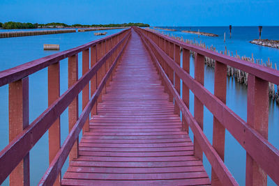 Empty footbridge over sea against sky