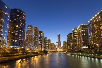 Canal amidst illuminated buildings against clear blue sky at night