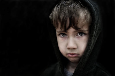 Close-up portrait of boy in hood against black background