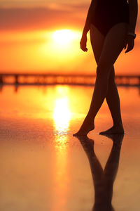 Low section of woman walking on beach during sunset