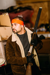 Young man looking away while holding gun at home