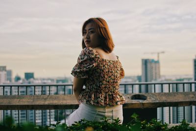 Young woman looking away while standing by railing against sky