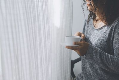 Midsection of woman holding coffee cup standing at home