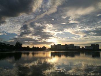 Silhouette buildings by lake against sky during sunset