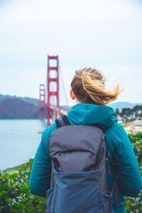 Rear view of backpack woman standing against golden gate bridge