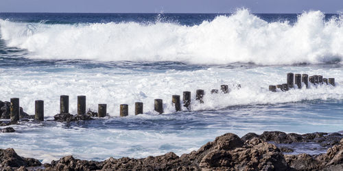 Waves splashing on rocks at sea against sky