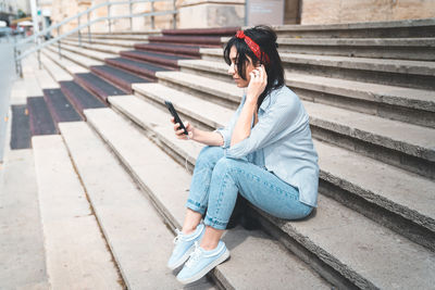 Young woman using phone while sitting on staircase