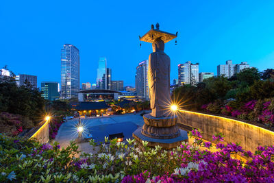 Illuminated statue by buildings against blue sky