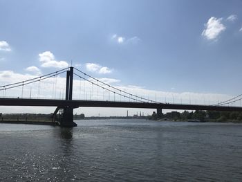 View of suspension bridge over river against cloudy sky