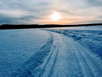 Snow covered landscape against sky during sunset