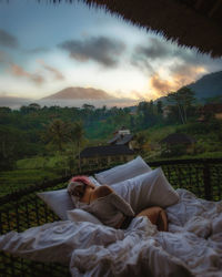 Woman resting on field against sky during sunset