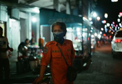 Portrait of man standing on illuminated street at night