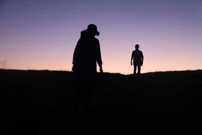 Silhouette of people standing on field at sunset
