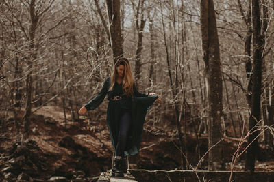 Woman standing by bare trees in forest