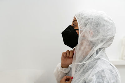 Side view of female medical specialist putting on protective suit with face mask and protective cap while preparing for work during coronavirus pandemic