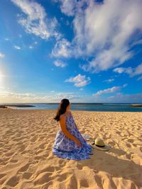 Rear view of woman standing at beach against sky