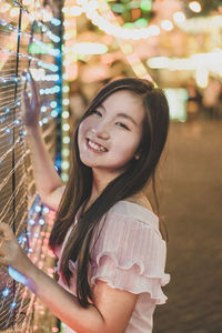 Portrait of smiling young woman standing at amusement park during night