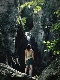 Rear view of woman standing on rock in forest