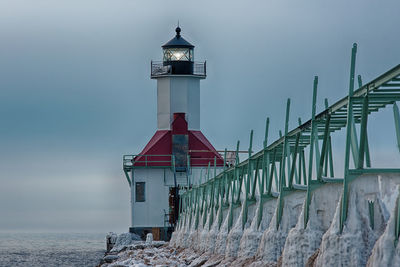 Lighthouse by sea against sky during winter