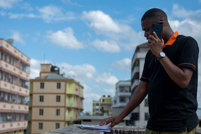 Man using smart phone at rooftop against sky