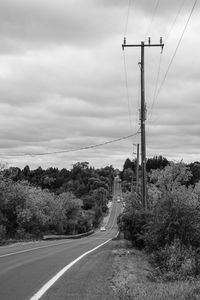 Road by electricity pylon against sky
