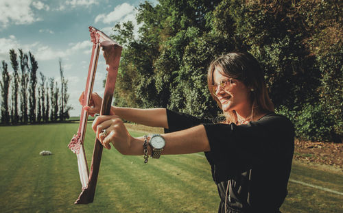 Smiling young woman holding picture frame outdoors