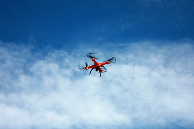 Orange flying drone in blue cloudy sky