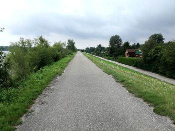 Country road amidst trees against sky