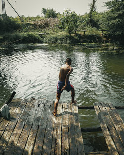 Rear view of shirtless man on pier over lake