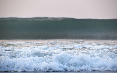 Waves rushing towards shore against sky