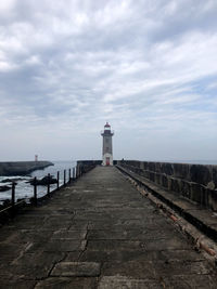 Lighthouse on footpath by sea against sky